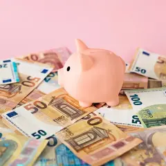 Różowa świnka-skarbonka na stosie banknotów euro. Symbol oszczędzania i budowania kapitału na rachunek oszczędnościowy.