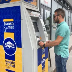 Mężczyzna korzysta z bankomatu Euronet, aby wypłacić pieniądze. Na urządzeniu widnieje napis "bankomat".
