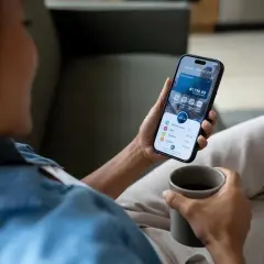 Kobieta z kubkiem kawy sprawdza na telefonie saldo konta bankowego. Aplikacja pokazuje dostępne środki i szczegóły wydatków.