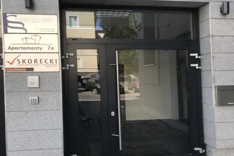 Wejście do budynku z tabliczkami informacyjnymi, w tym "SKORECKI KANCELARIA DORADCY FINANSOWEGO".