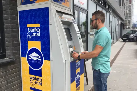 Mężczyzna korzysta z bankomatu Euronet, aby wypłacić pieniądze. Na urządzeniu widnieje napis "bankomat".