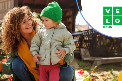 Uśmiechnięta mama z dzieckiem w ogrodzie. VeloBank lokaty na nowe środki to pewność przyszłości.