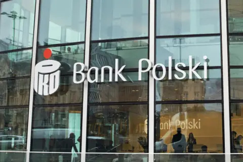 Logo PKO Bank Polski na szklanej fasadzie. Widać odbicia ludzi i miasta.