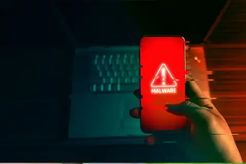 Dłoń trzyma smartfon z czerwonym ekranem i ostrzeżeniem o złośliwym oprogramowaniu. To może być początek oszustwa na blik.