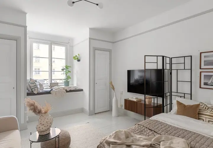 Przytulne mieszkanie bezczynszowe z wygodną kanapą przy oknie, łóżkiem i telewizorem.