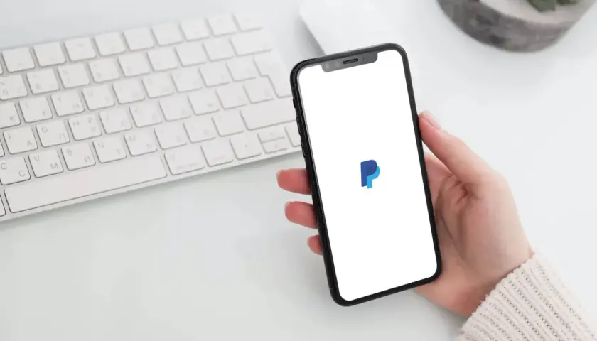 Dłoń trzyma smartfon z logo PayPal. Czy PayPal jest darmowy? Sprawdź na telefonie, obok klawiatury.