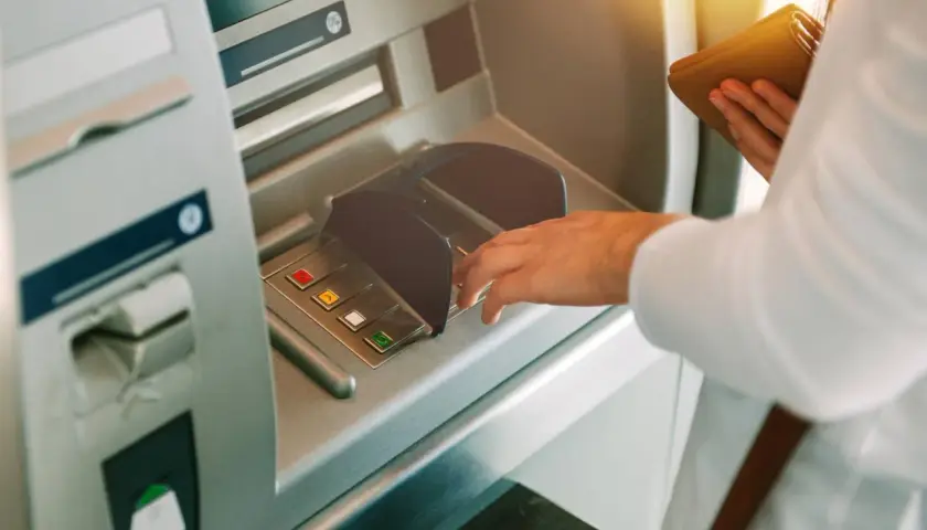 Dłoń wpisuje PIN przy bankomacie, mając nadzieję, że nie zniknęły pieniądze z konta.