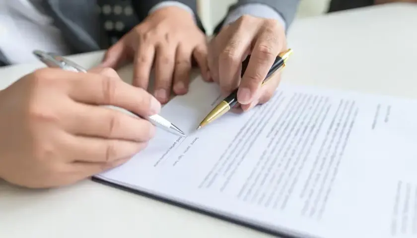 Dwie osoby podpisują dokument, trzymając długopisy.
