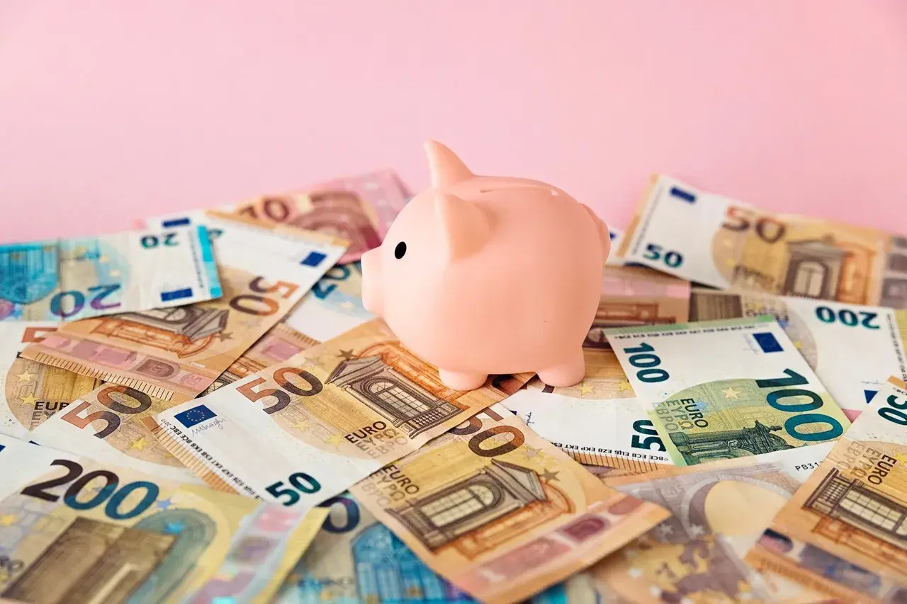 Różowa świnka-skarbonka na stosie banknotów euro. Symbol oszczędzania i budowania kapitału na rachunek oszczędnościowy.