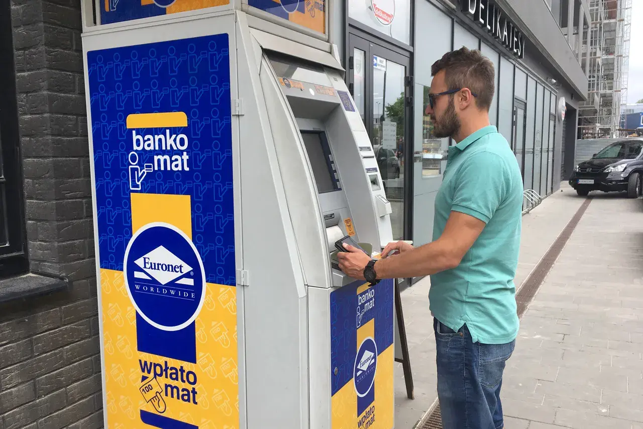 Mężczyzna korzysta z bankomatu Euronet, aby wypłacić pieniądze. Na urządzeniu widnieje napis "bankomat".