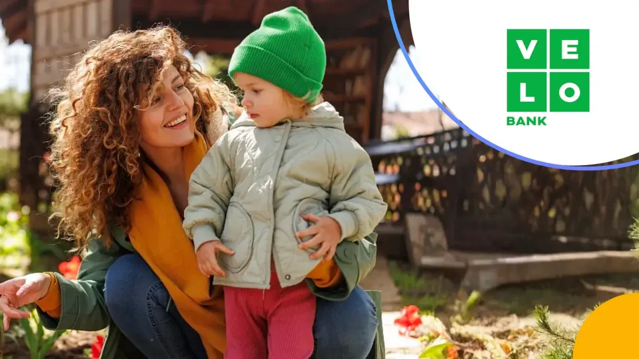 Uśmiechnięta mama z dzieckiem w ogrodzie. VeloBank lokaty na nowe środki to pewność przyszłości.