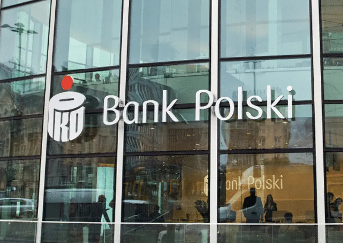 Logo PKO Bank Polski na szklanej fasadzie. Widać odbicia ludzi i miasta.