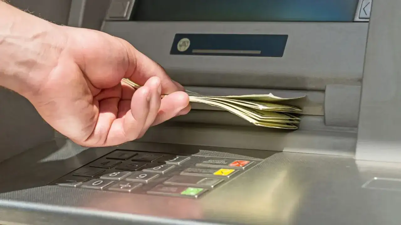 Dłoń odbiera plik banknotów z bankomatu. Prosty sposób, jak wypłacić pieniądze z bankomatu.