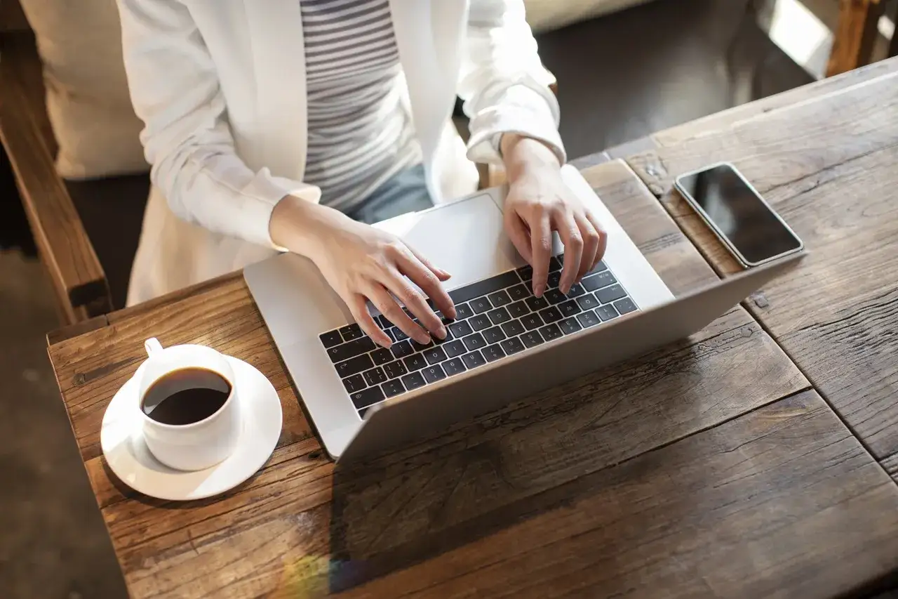 Kobieta pracuje na laptopie, realizując nest bank sesje przychodzące. Obok kawa i telefon.
