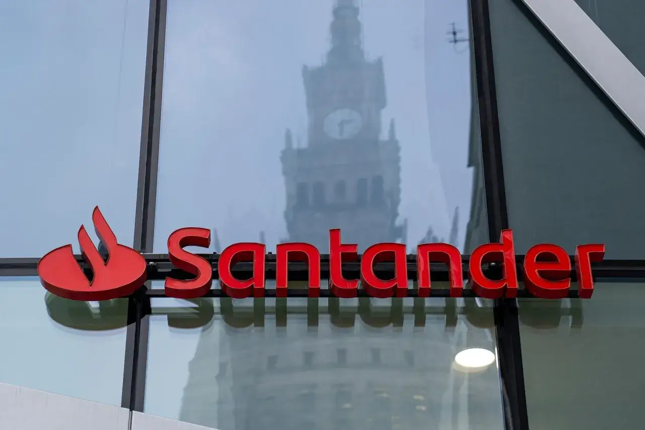 Czerwony napis Santander na szkle, w którym odbija się wieżowiec. Wpływy banku są widoczne w miejskim krajobrazie.