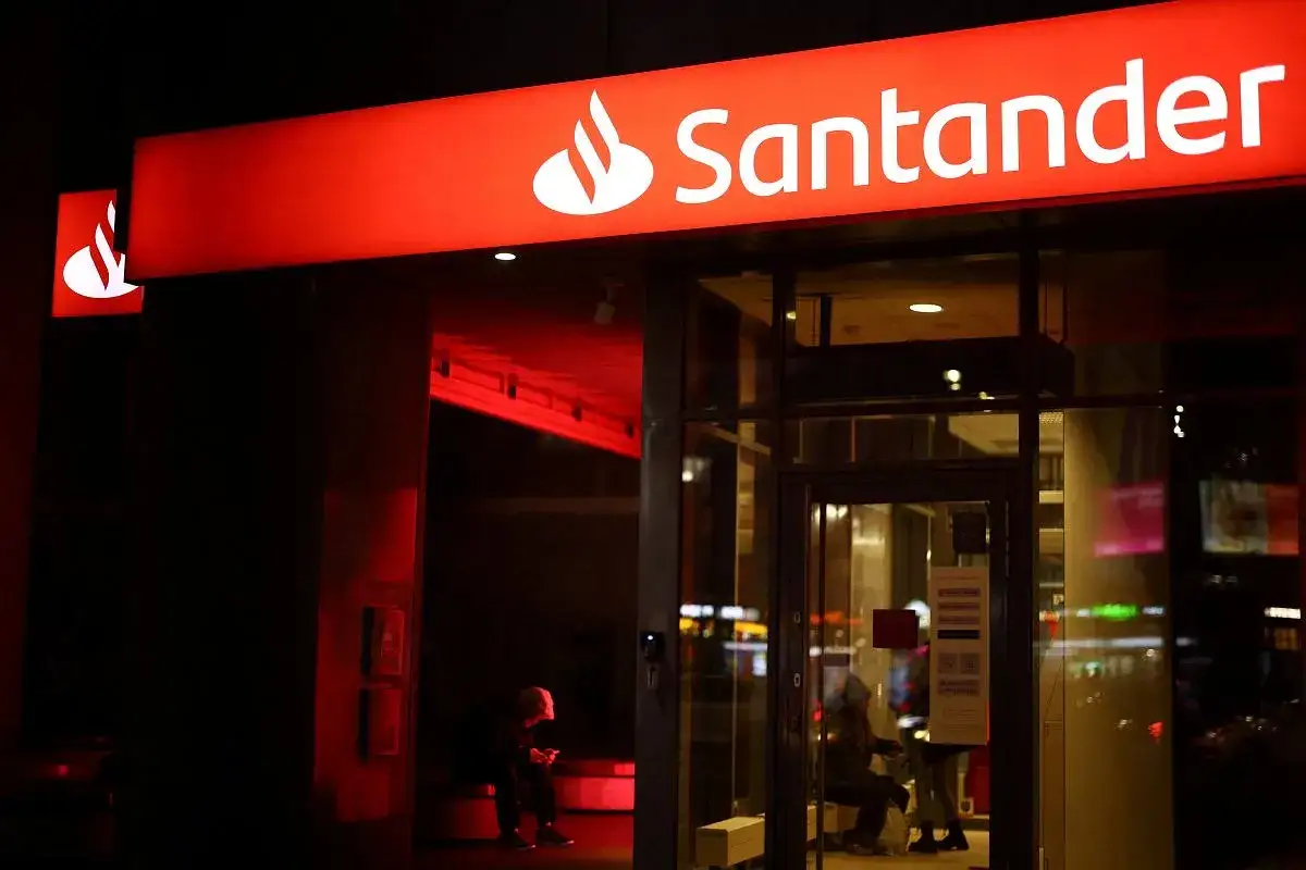 Czerwony neon Santander nocą. W środku i na zewnątrz widać ludzi, a czerwone światło podkreśla atmosferę. Wpływy Santander są widoczne w miejskim krajobrazie.
